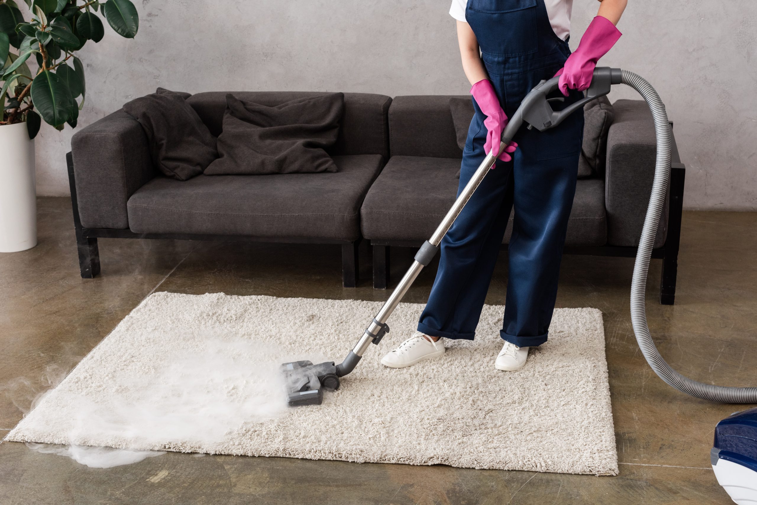 cropped view of cleaner in overalls and rubber gloves using vacuum cleaner with hot steam on carpet