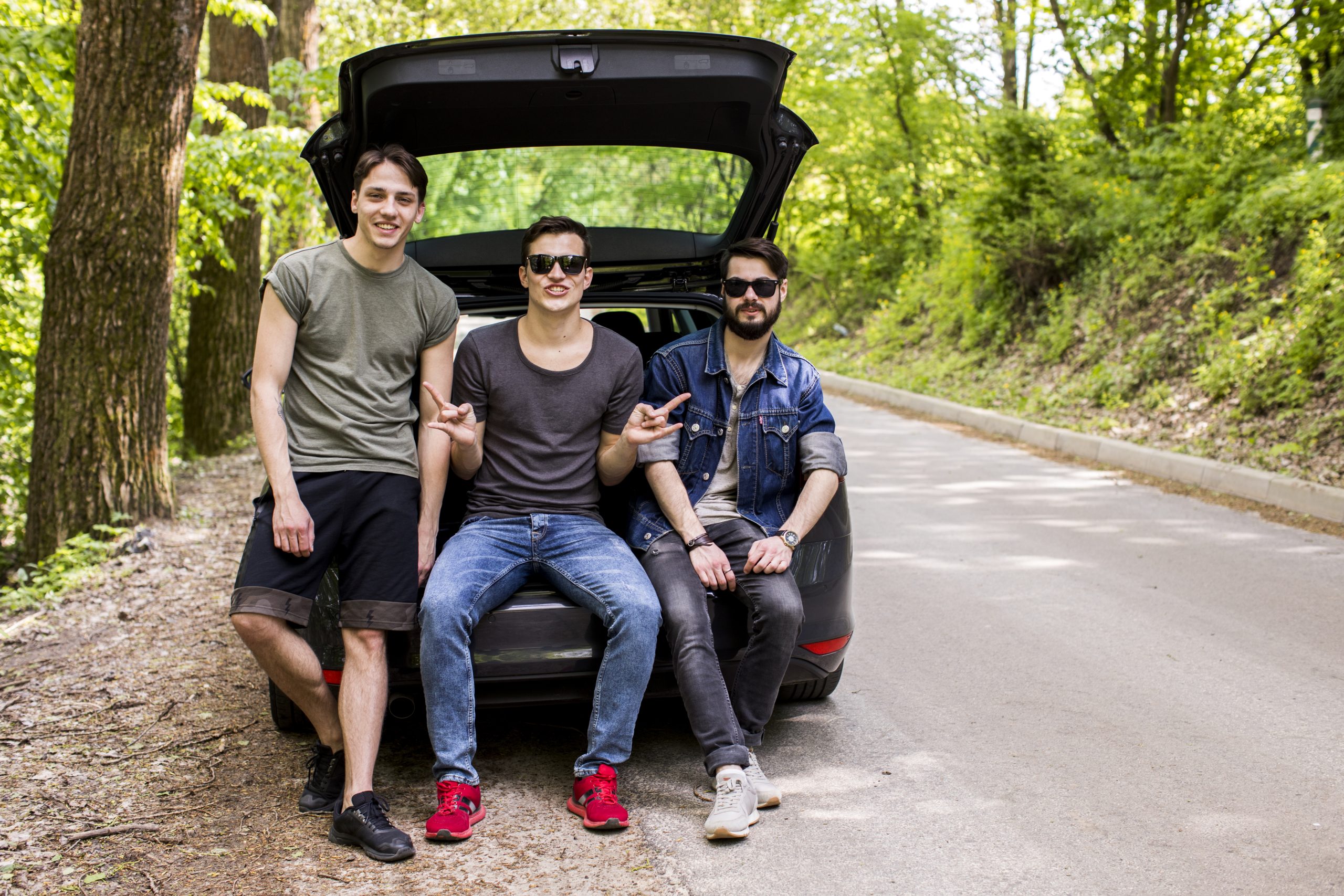 joyful young guys sitting trunk forest road